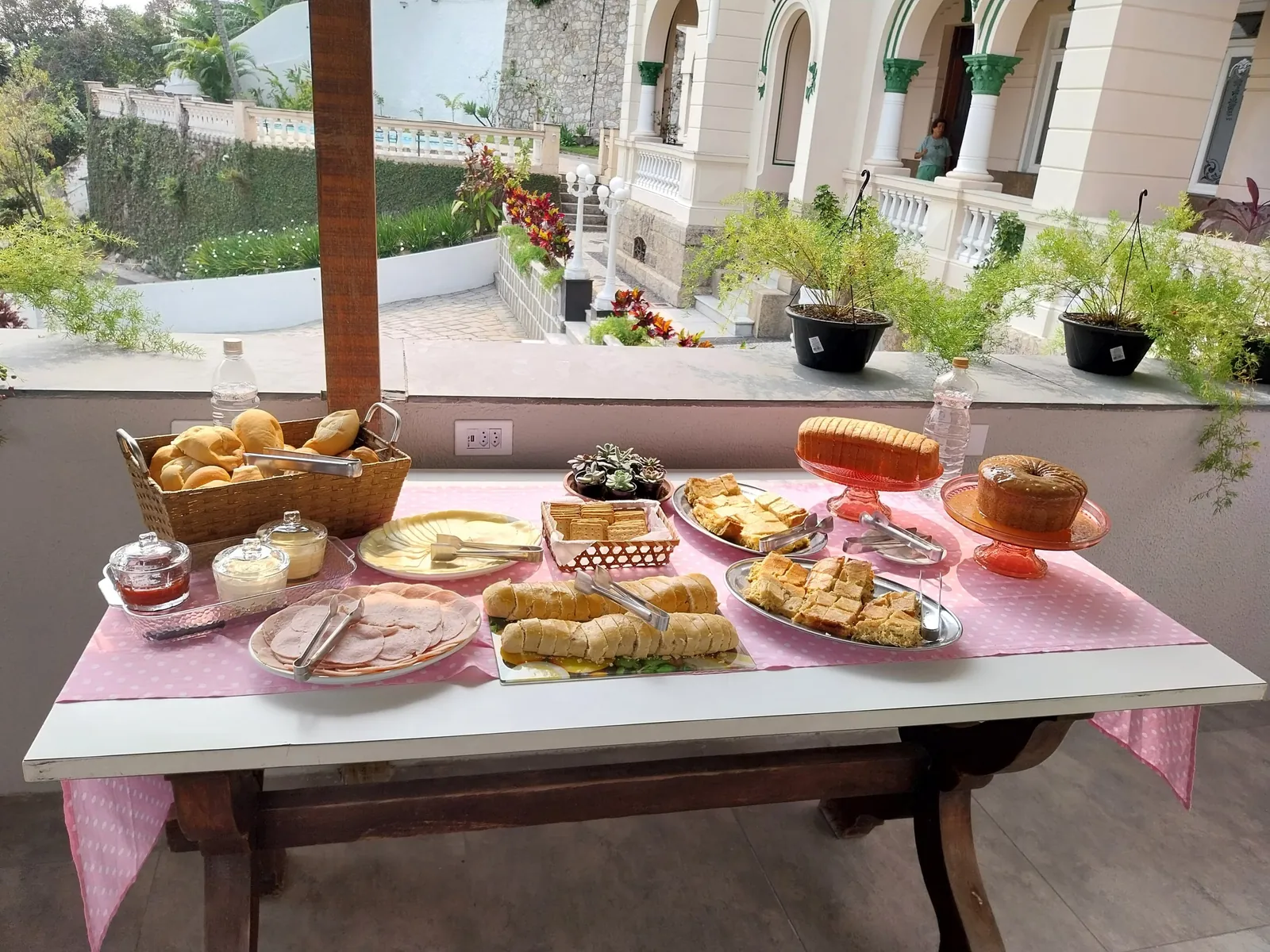 Mesa posta de café da manhã com pães, bolos e frutas.