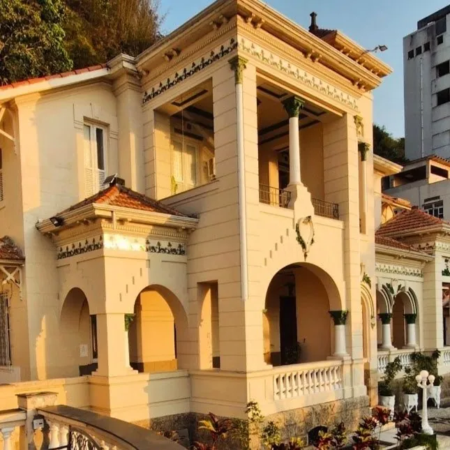 Detalhe da fachada do casarão ao entardecer, com arcos e ornamentos verdes.