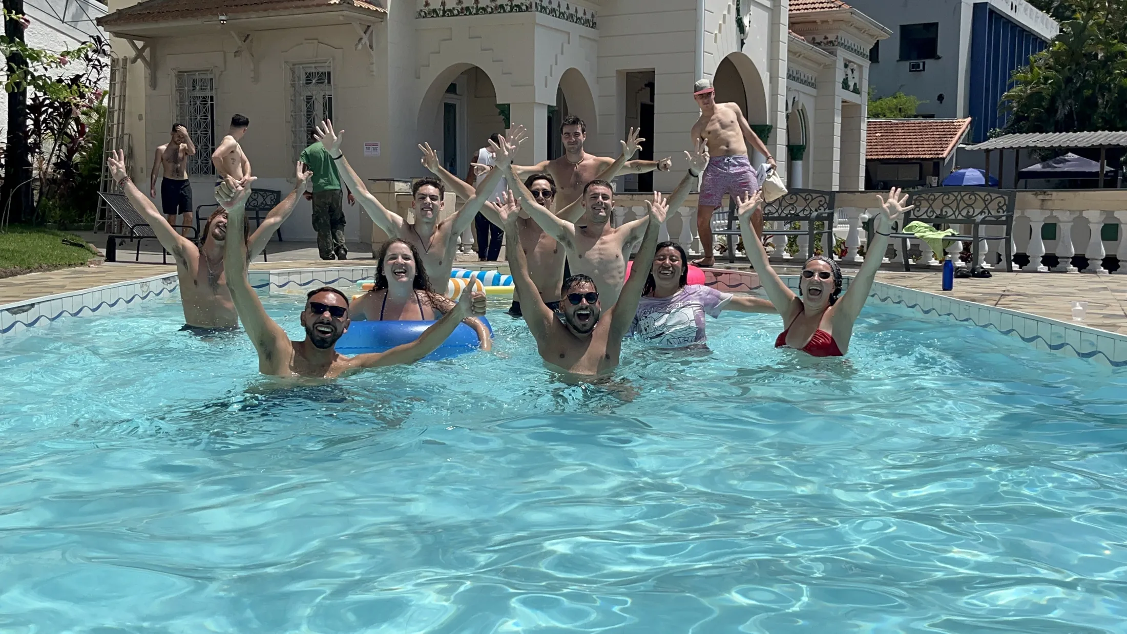 Hóspedes na piscina do hostel, com o casarão ao fundo.