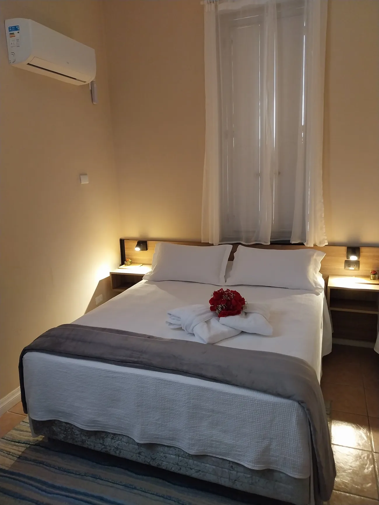 Quarto de casal privativo com cama queen, enxoval branco e luminárias de leitura.